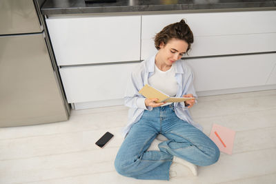 Portrait of young woman using mobile phone while standing against wall