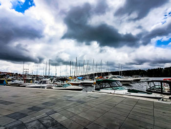 Sailboats moored at harbor against cloudy sky