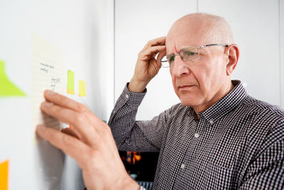 Senior man brainstorming while looking at adhesive note at home