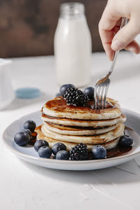 Woman sticking a fork into a stack of homemade pancakes with berries