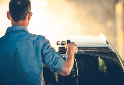 Rear view of man holding mobile phone while standing in car