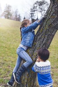 Girl with brother climbing tree on field