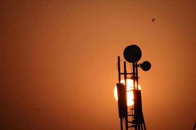 Low angle view of silhouette repeater tower against orange sky