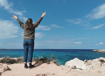 Rear view of woman walking on beach against sky