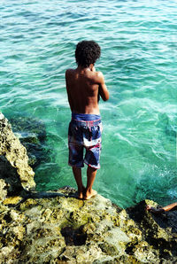 Rear view of shirtless boy standing in sea