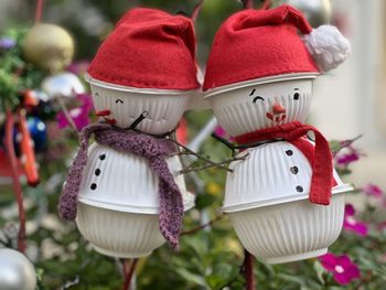 Close-up of two snowmen made from paper cups on a tree.