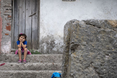 Portrait of cute girl sitting on staircase against wall