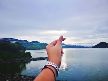 Midsection of hand against sea against sky