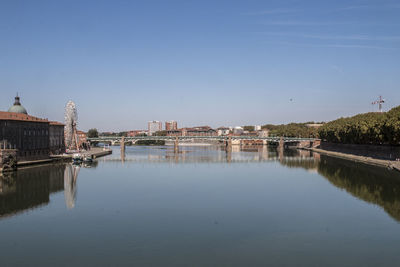 Buildings by river against clear blue sky