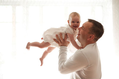 Father and daughter laughing on light window, toddler on hands. happy loving family. 