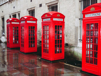 Red telephone booth on sidewalk against building in city