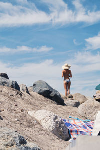 Low angle view of young woman in bikini standing on rock against sky