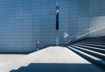 Rear view of person walking on footpath against building