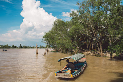 Man sitting on boat in river against sky