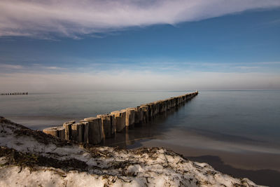 Wooden posts on beach by sea against sky