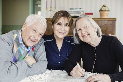 Portrait of smiling caretaker and senior people solving crossword puzzle at nursing home