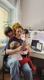 Woman working at her home office with a laptop and a smartphone surrounded with 3 small children