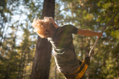 Low angle view of boy sitting on swing outdoors