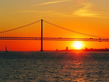 Bridge over calm sea against orange sky