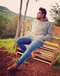 Young man looking away while sitting on bench