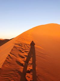 Shadow of man on sand dune against clear sky