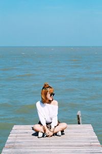 Woman sitting on pier by sea against clear sky