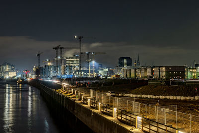 Illuminated city by river against sky at night