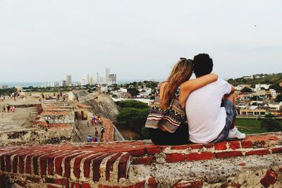 Rear view of couple sitting on retaining wall at castle against clear sky