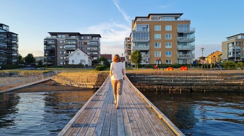 Rear view of woman standing on pier amidst buildings against sky