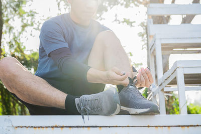 Low section of athlete tying shoelace while sitting at park during sunny day
