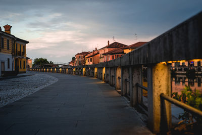 Empty road amidst buildings against sky during sunset