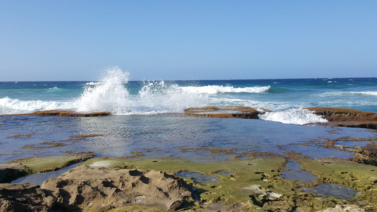 water, sea, horizon over water, wave, splashing, clear sky, motion, surf, beach, scenics, shore, beauty in nature, nature, rock - object, copy space, blue, tranquil scene, tranquility, idyllic, sky