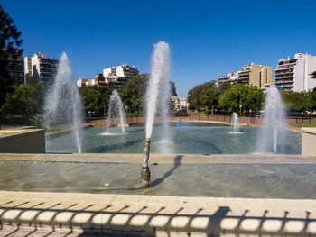 Fountain by swimming pool in city against sky