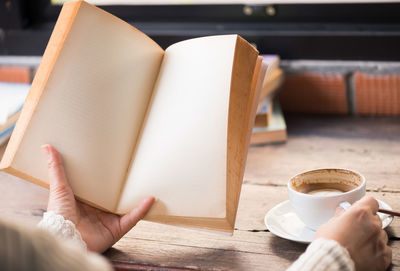 Close-up of woman holding coffee cup on table