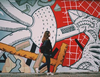 Full length of woman standing against graffiti wall