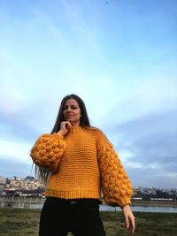 Portrait of smiling young woman in sweater against sky