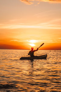 Silhouette man in boat in sea against sky during sunset
