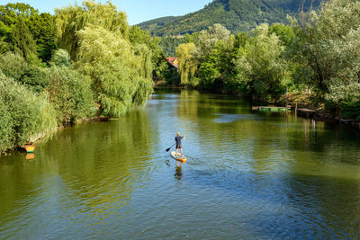 Rear view of man paddling on sup board on river.