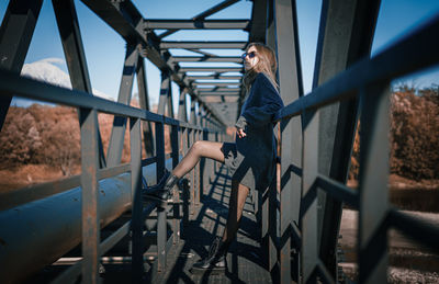 Side view of woman standing on railing against bridge