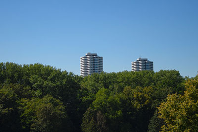 Low angle view of tree by building against clear blue sky