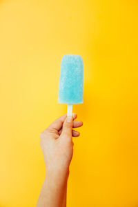 Close-up of hand holding popsicle against yellow background