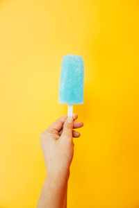 Close-up of hand holding ice cream cone against yellow background