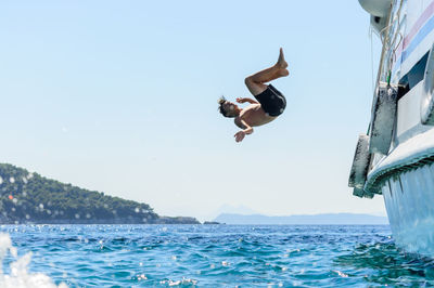 Teenage boy diving into sea against clear sky