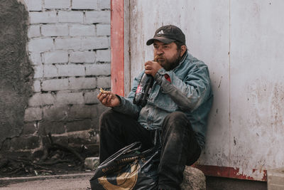 Full length of man sitting against wall