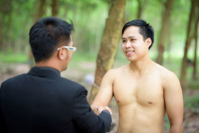 Smiling shirtless worker handshaking with manager on field