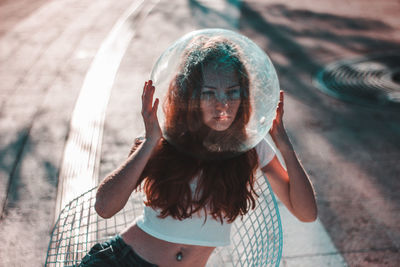 Fashionable young woman wearing glass helmet while sitting on modern chair at street