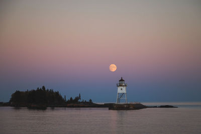 Full moon rising at twilight over the lighthouse on lake superior in grand marais, minnesota.