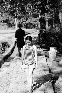 Young woman walking on footpath with man standing in background