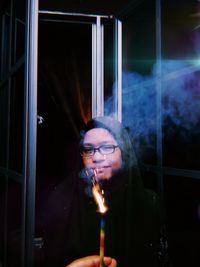 Cropped hand holding illuminated sparkler against woman at night