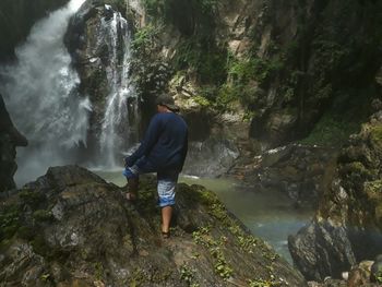 Rear view of woman standing on rock against waterfall